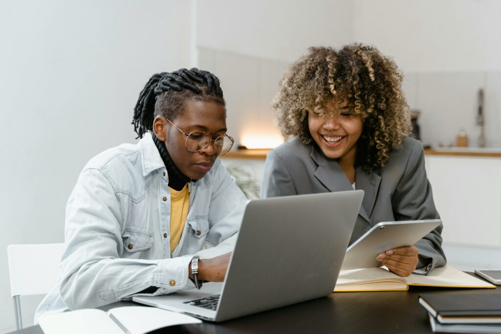 Two young adults engaged in conversation while sitting at a table with a laptop open between them.